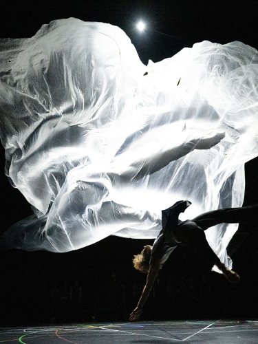 A dancer falling backward, a large white fabric floating behind him.