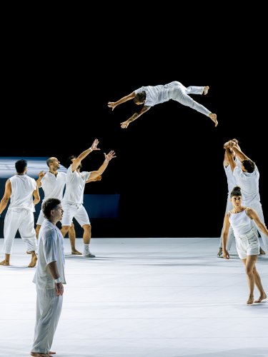 Dancers dressed in white, one in mid-leap