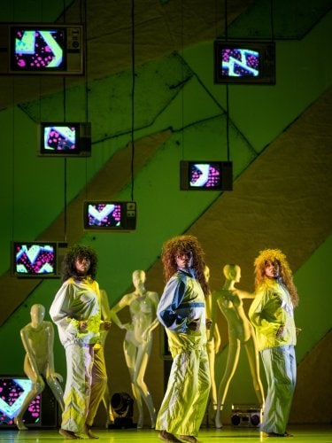 3 danseuses sur scène dans une lumière jaune devant des mannequins 