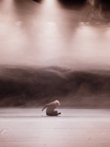 Dancer sitting in mist, under spotlights