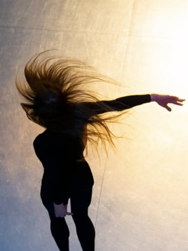 Dancer in black, hair flying, arm extended, on gradient blue background
