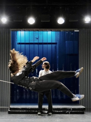 A dancer being pulled backward by a rope, with another person standing behind her