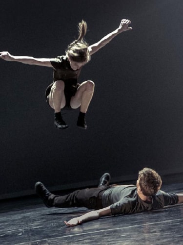 Dancer jumping over a dancer lying down, both dressed in black
