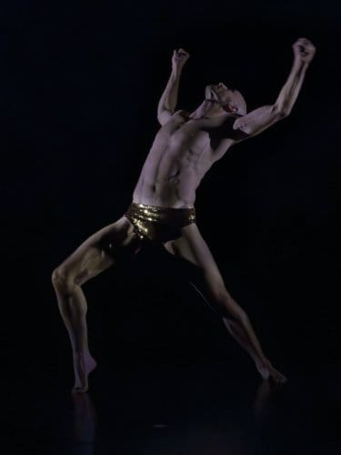 danseur bras levés, sur une scène sombre