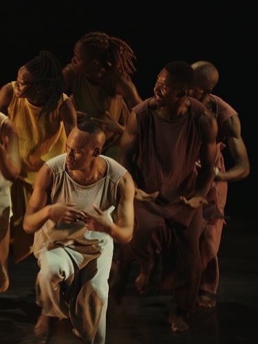 African dancers in traditional costumes of different solid colors on a black background