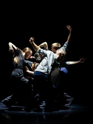 group of dancers in dynamic poses on a dark stage