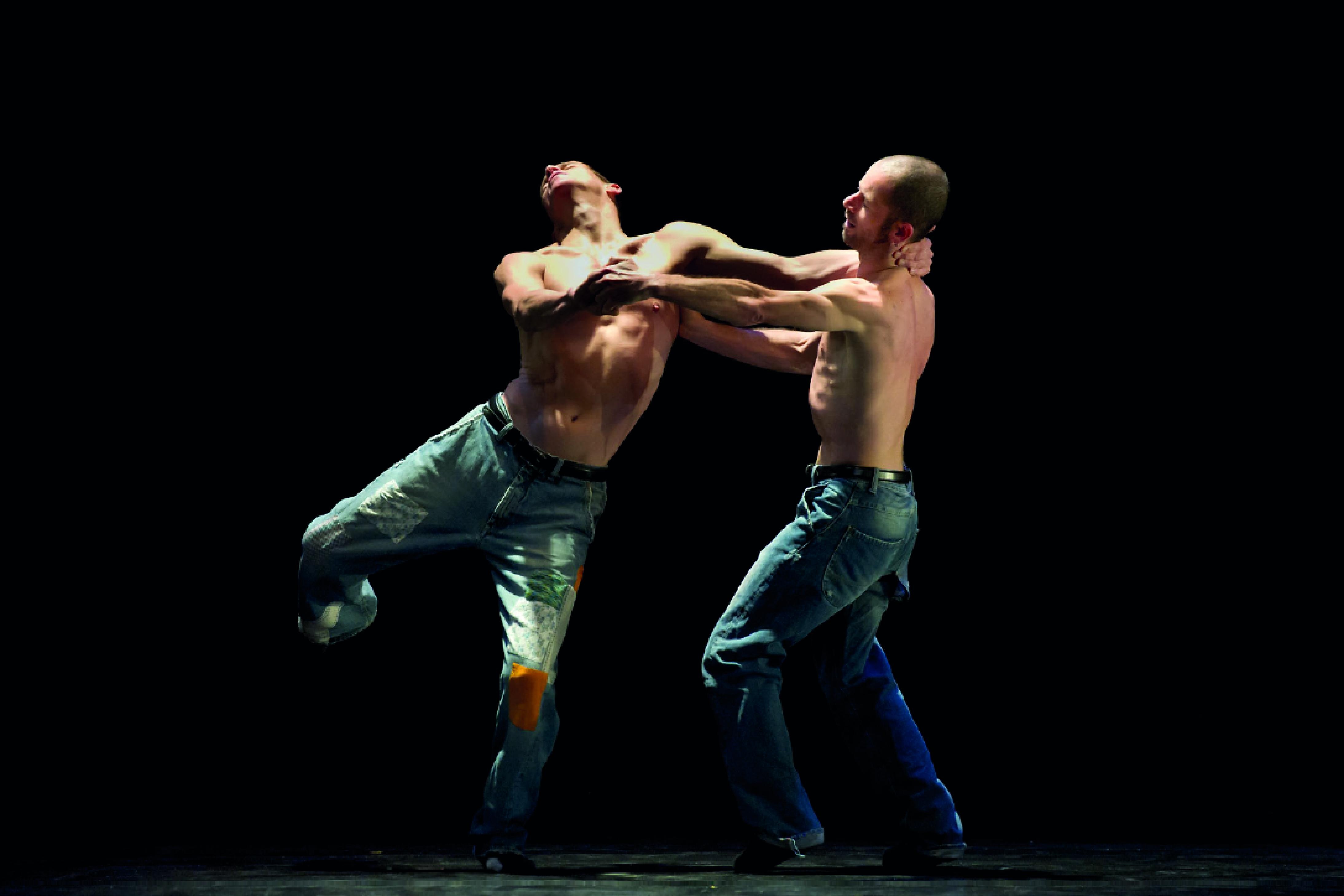 Two shirtless dancers in jeans, holding each other by the arms