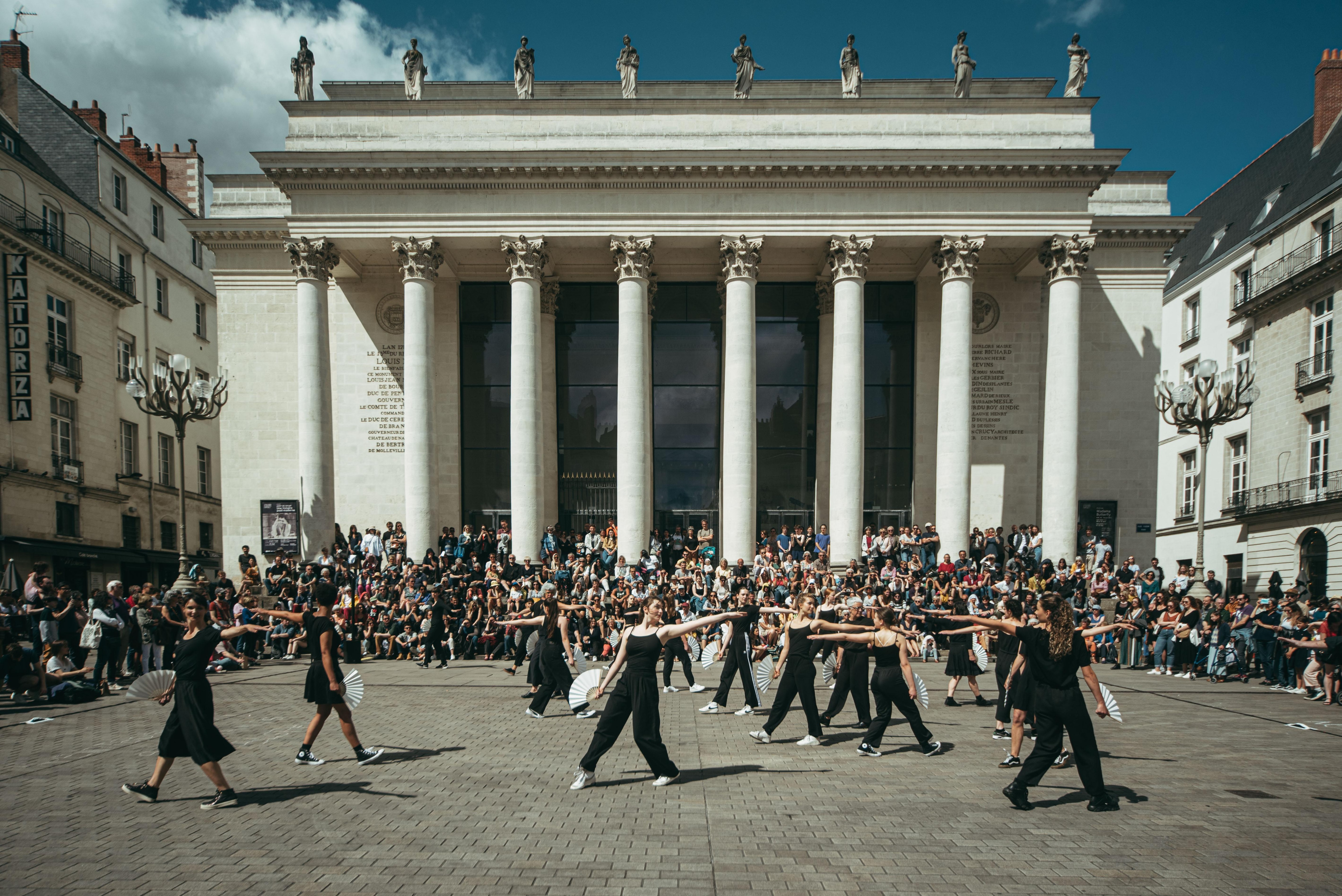 Dancers dressed in black, holding white fans in front of them, performing Andy De Groat's Fan Dance