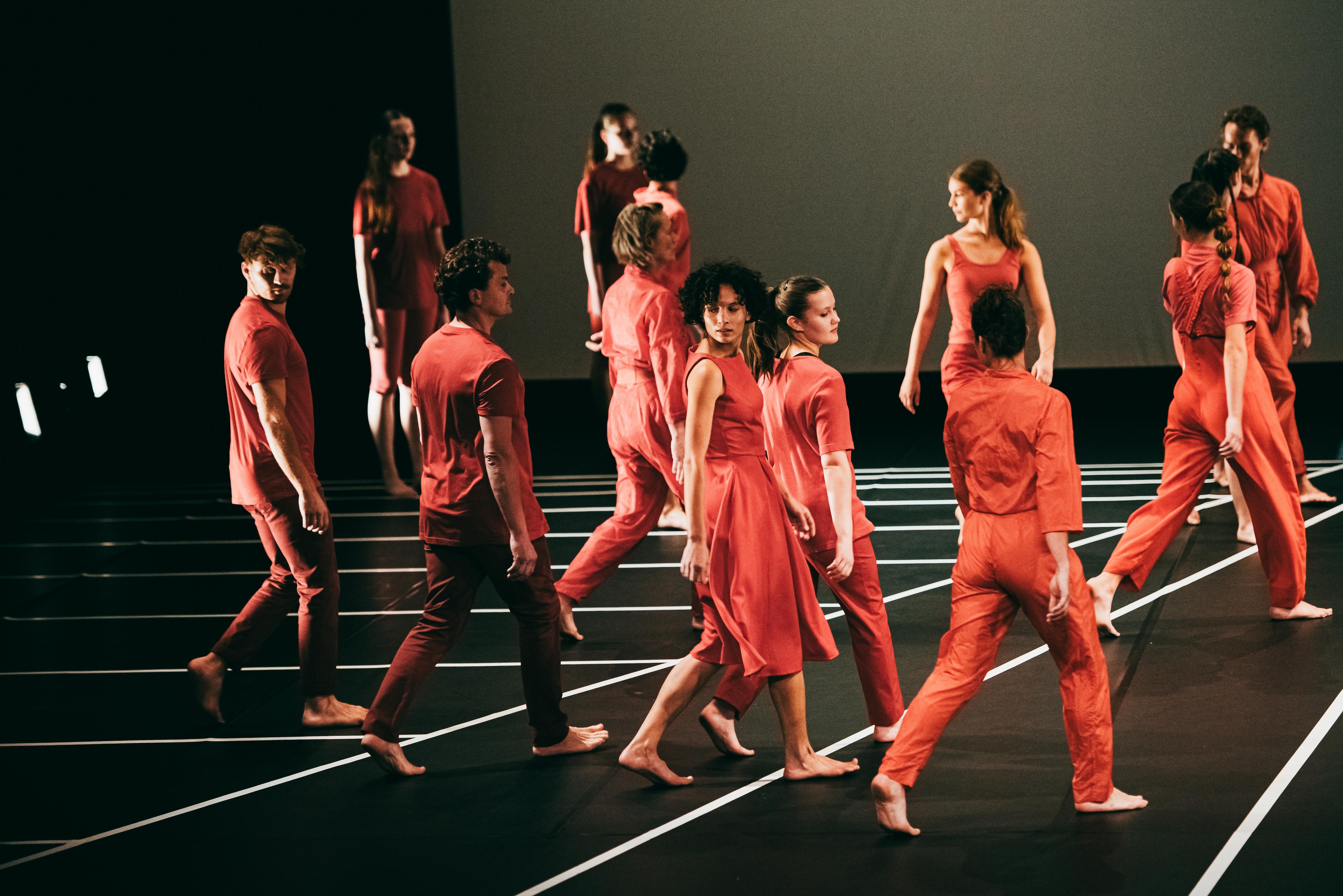 Dancers dressed in red, walking from the back or three-quarter view, performing Andy De Groat's Red Notes.