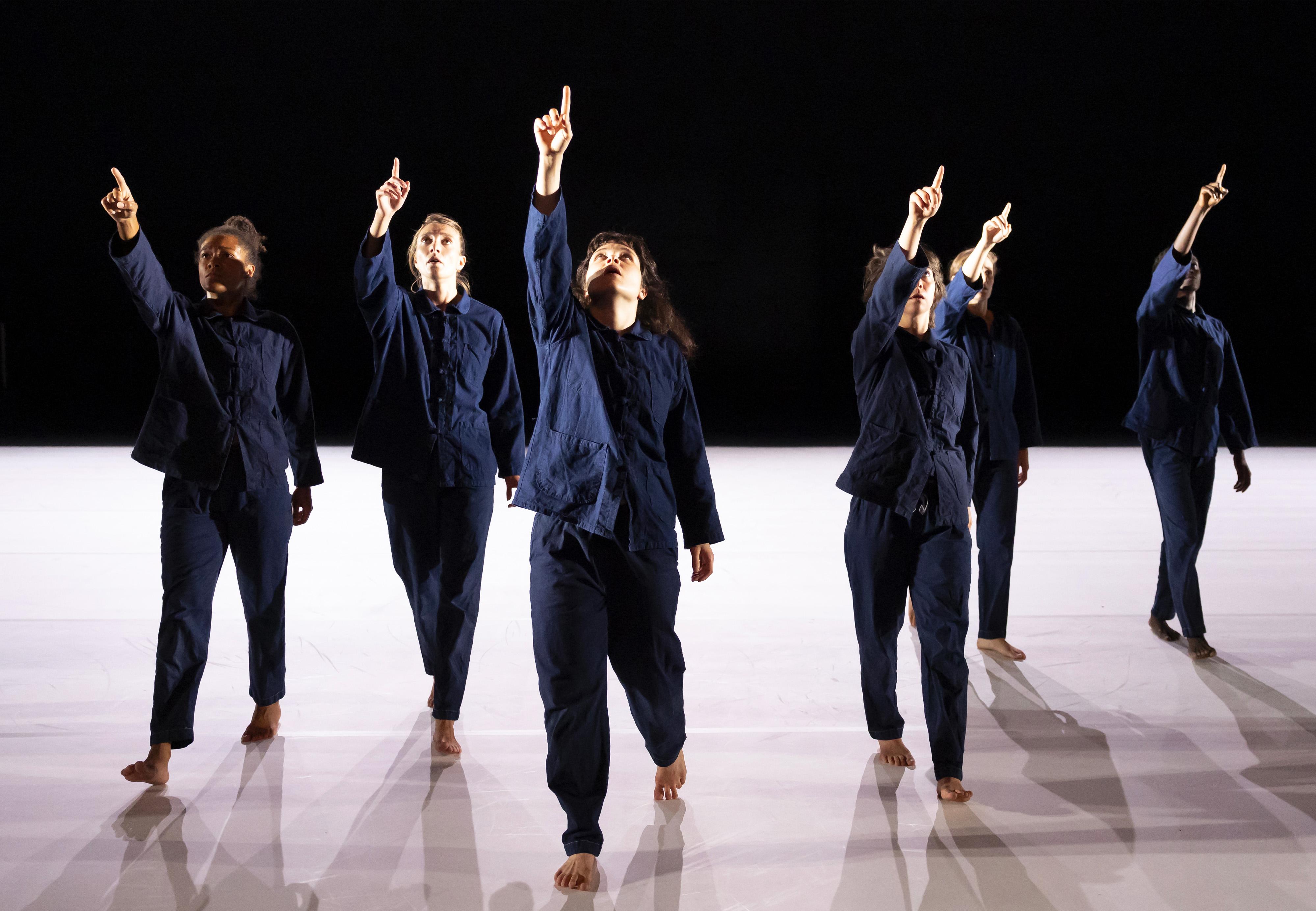 danseurs vêtus de bleus de travail, en ligne pointant le doigt vers le haut