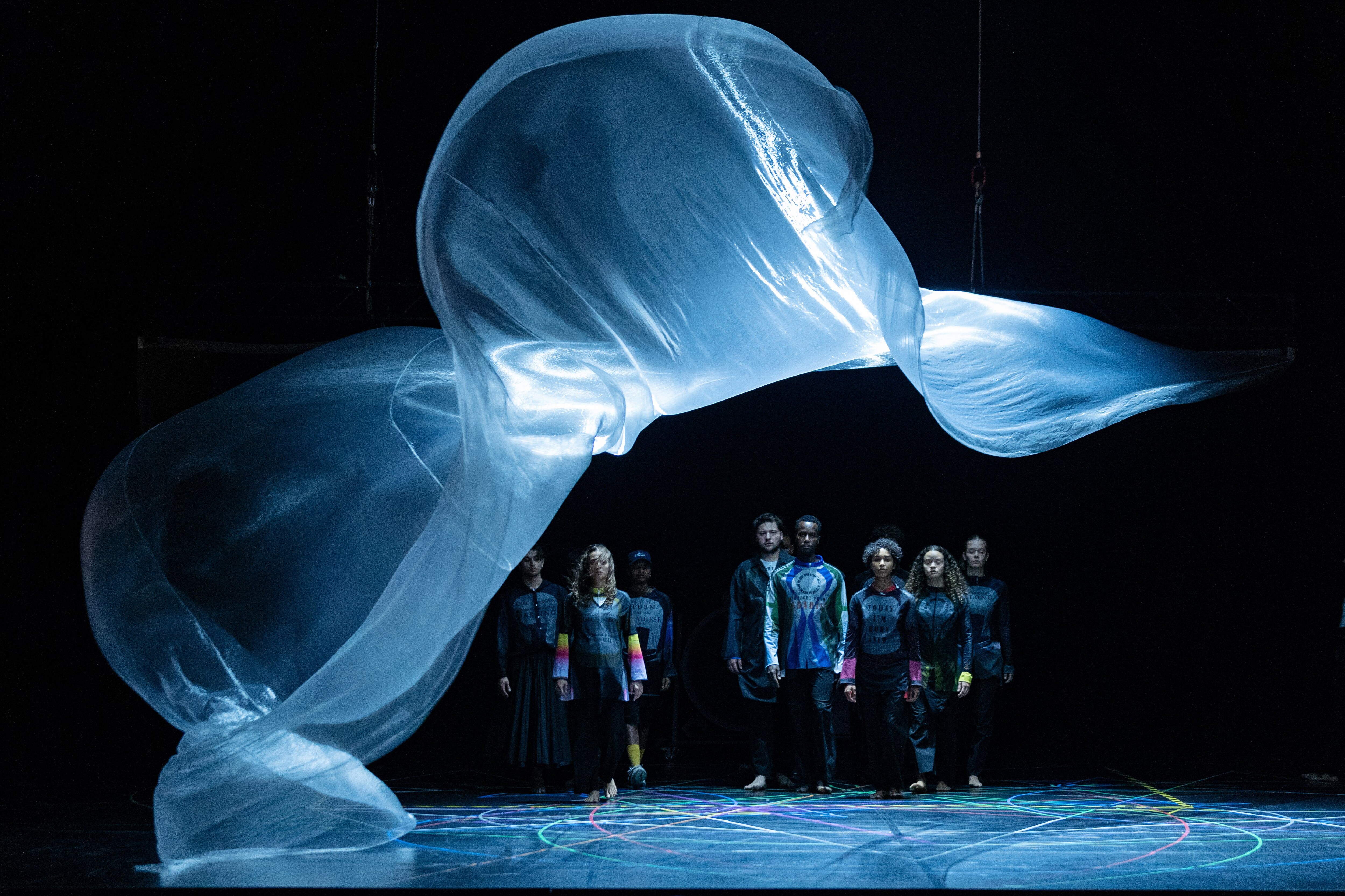 A group of dancers on stage beneath a large veil of light 