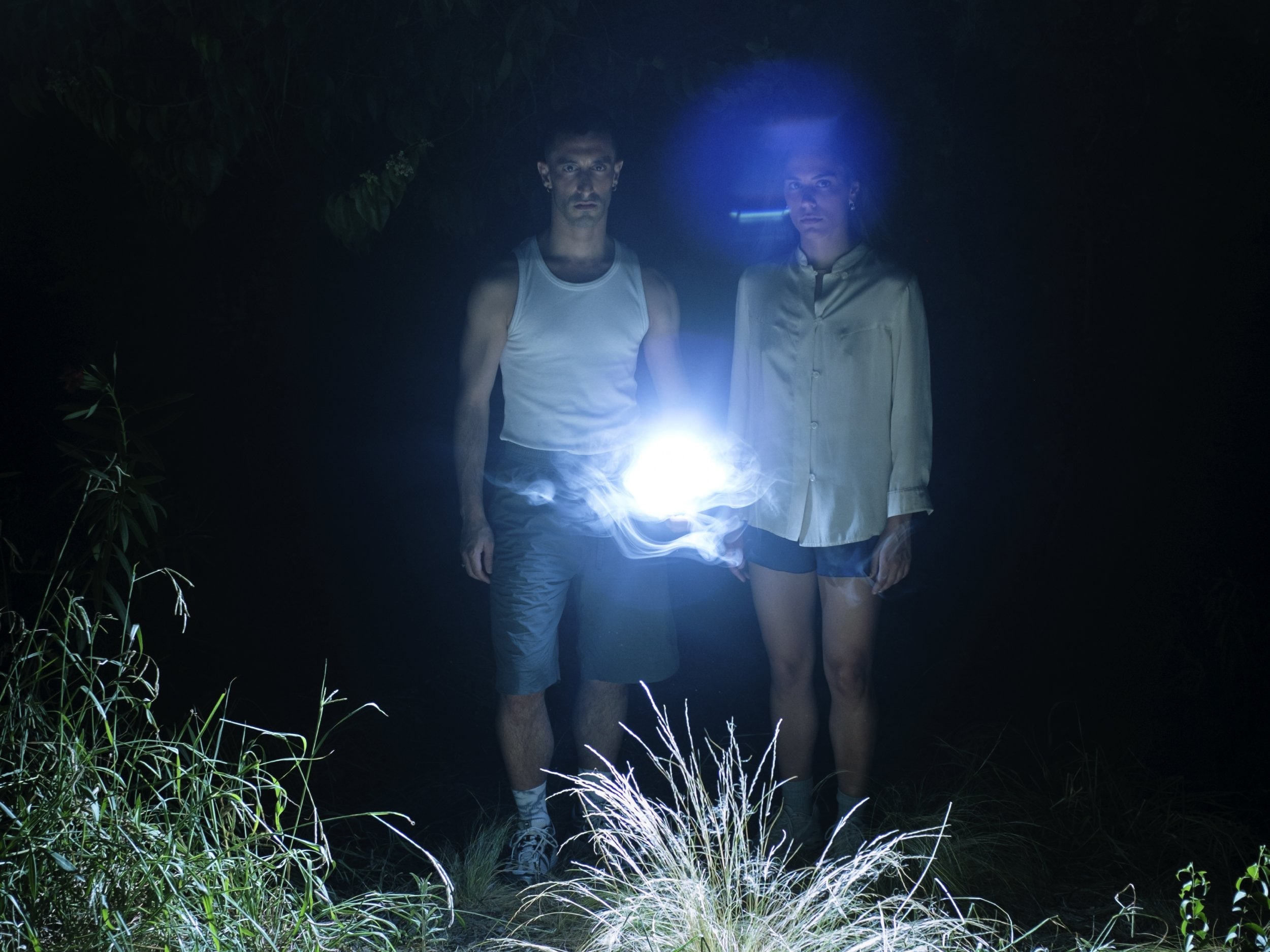 a man and a woman standing in the forest with a lamp on