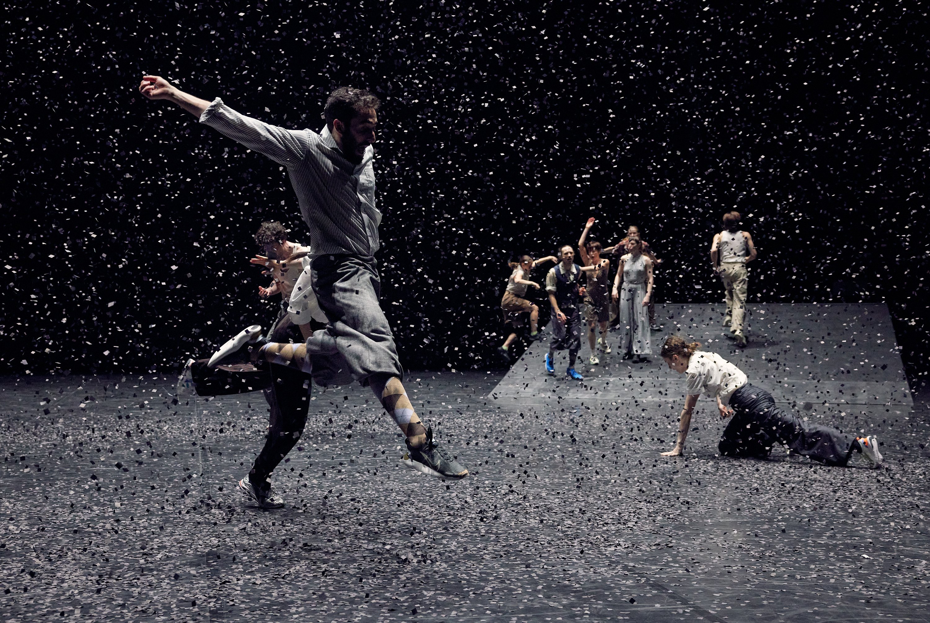 un groupe de danseurs dans le fond, trois danseurs en avant dont un dans les air sous des confettis