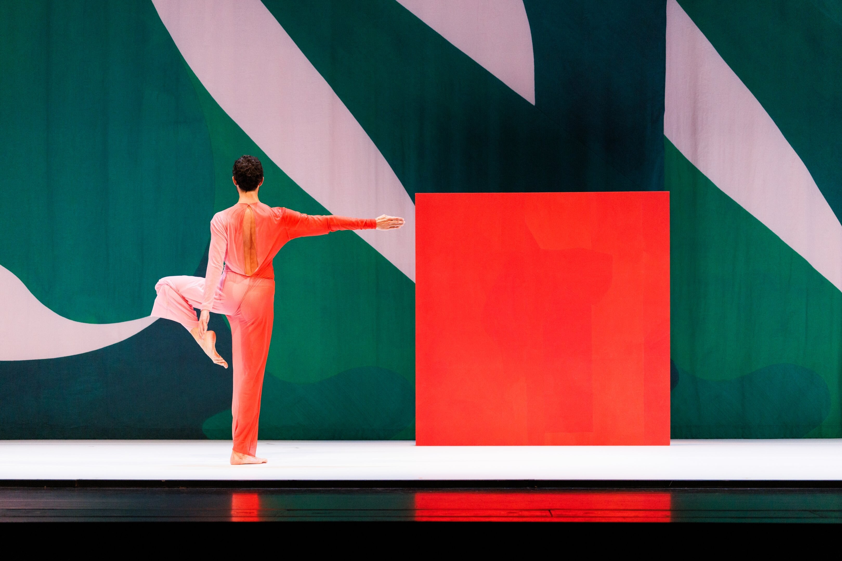 A dancer with their back turned, facing a giant painting with a red square.