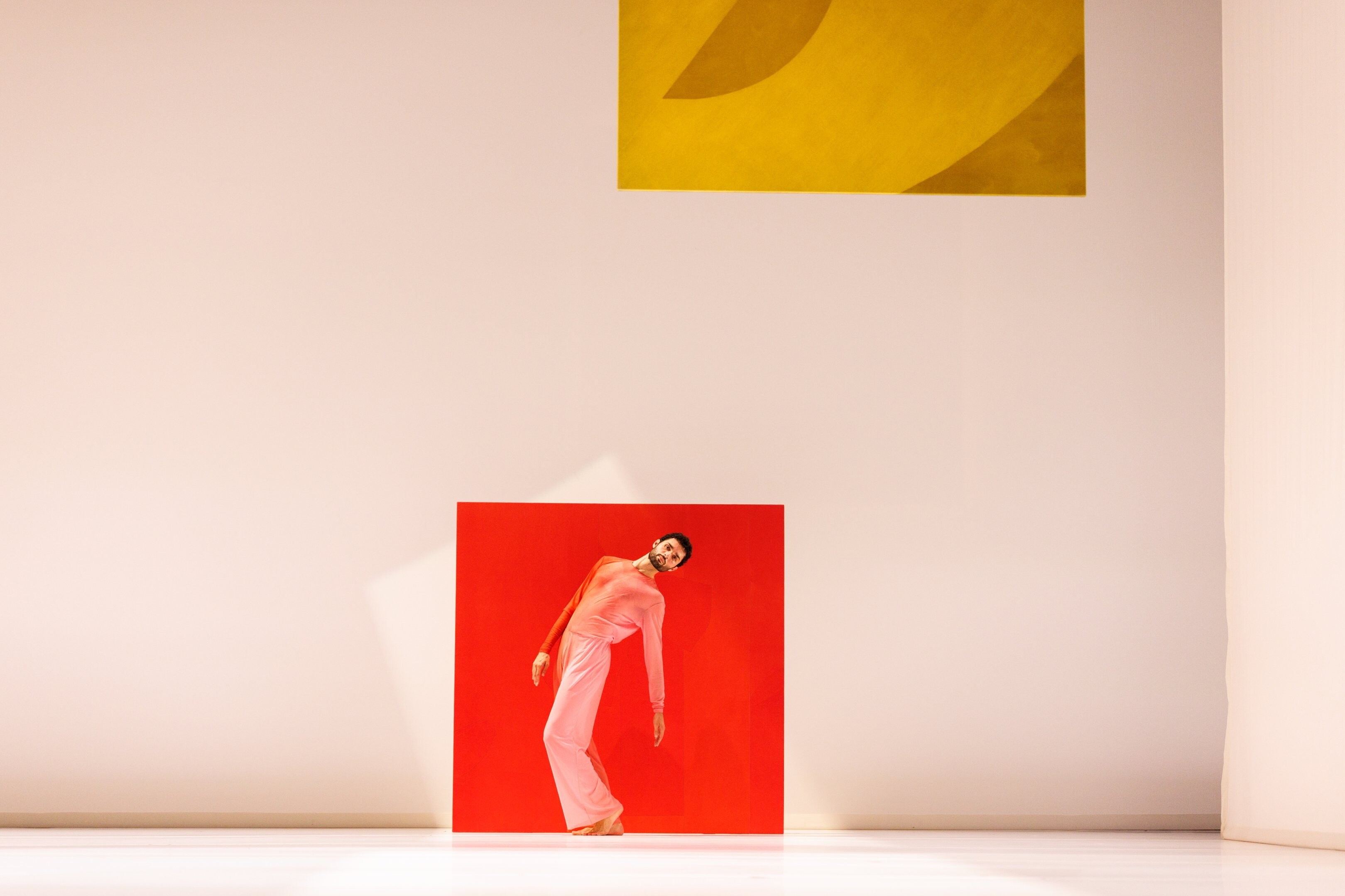 A dancer standing with their back arched in front of a painting of a red squareA dancer standing with his back arched in front of a painting of a red square