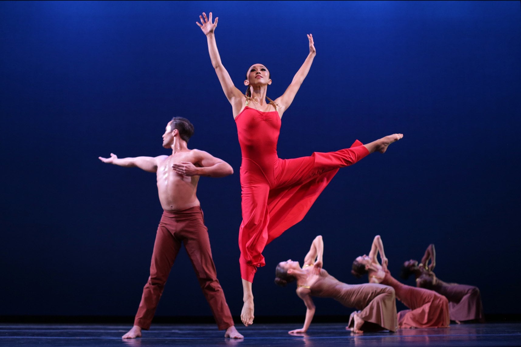 dancer in a red dress jumping with dancers behind