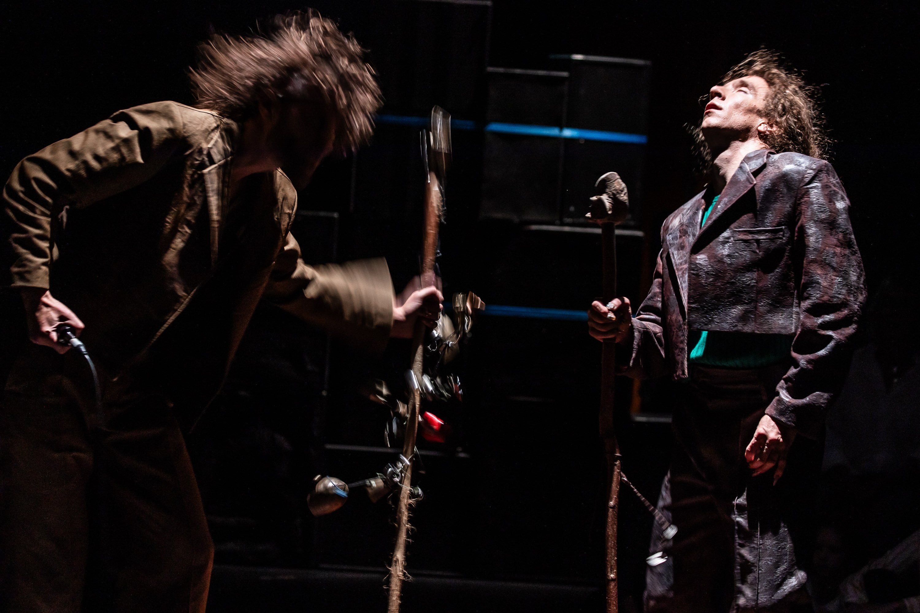 deux danseurs dans un espace sombre, l'un tape le sol avec un baton 