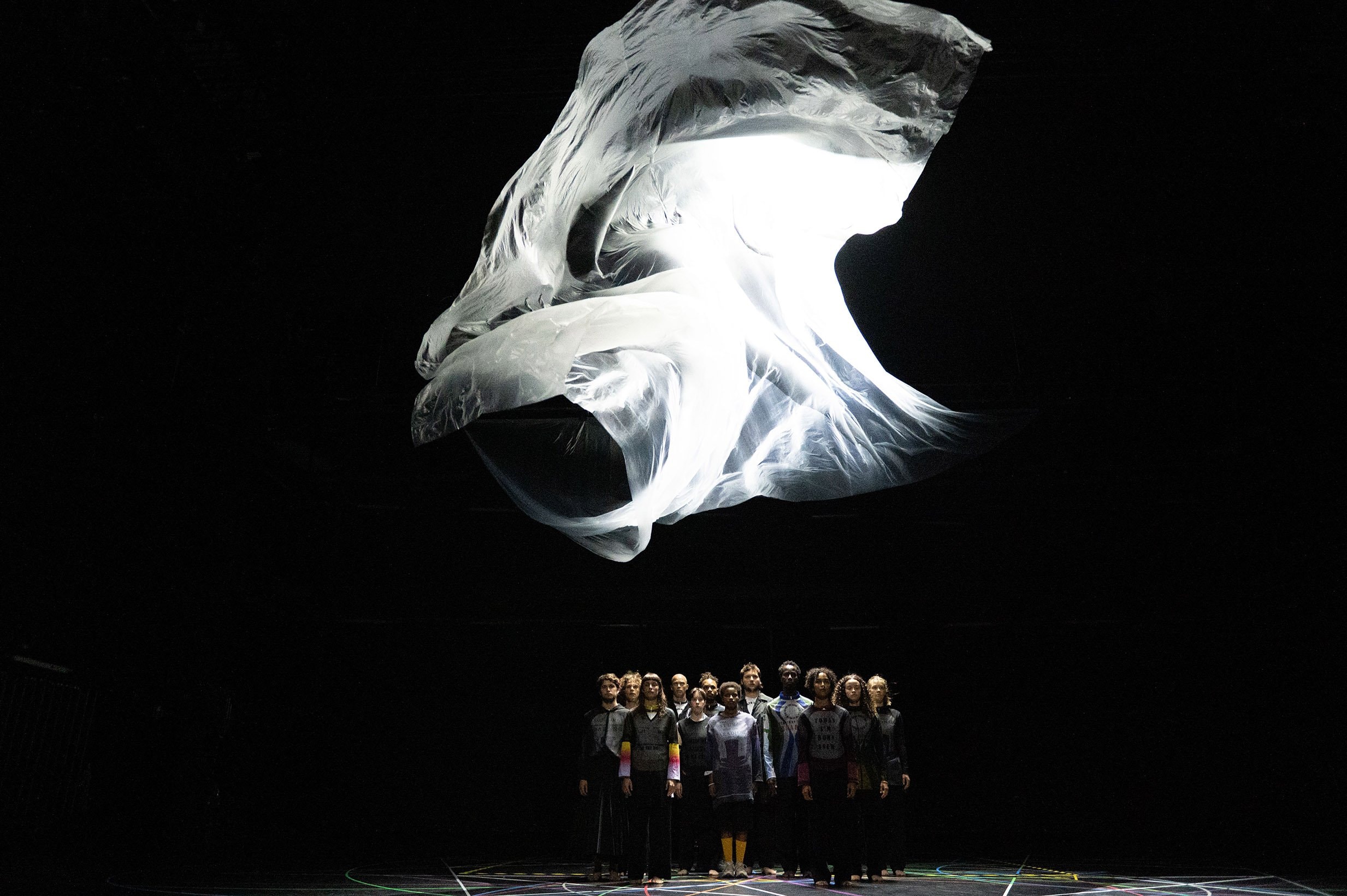 A group of standing dancers, with a large white fabric above them.