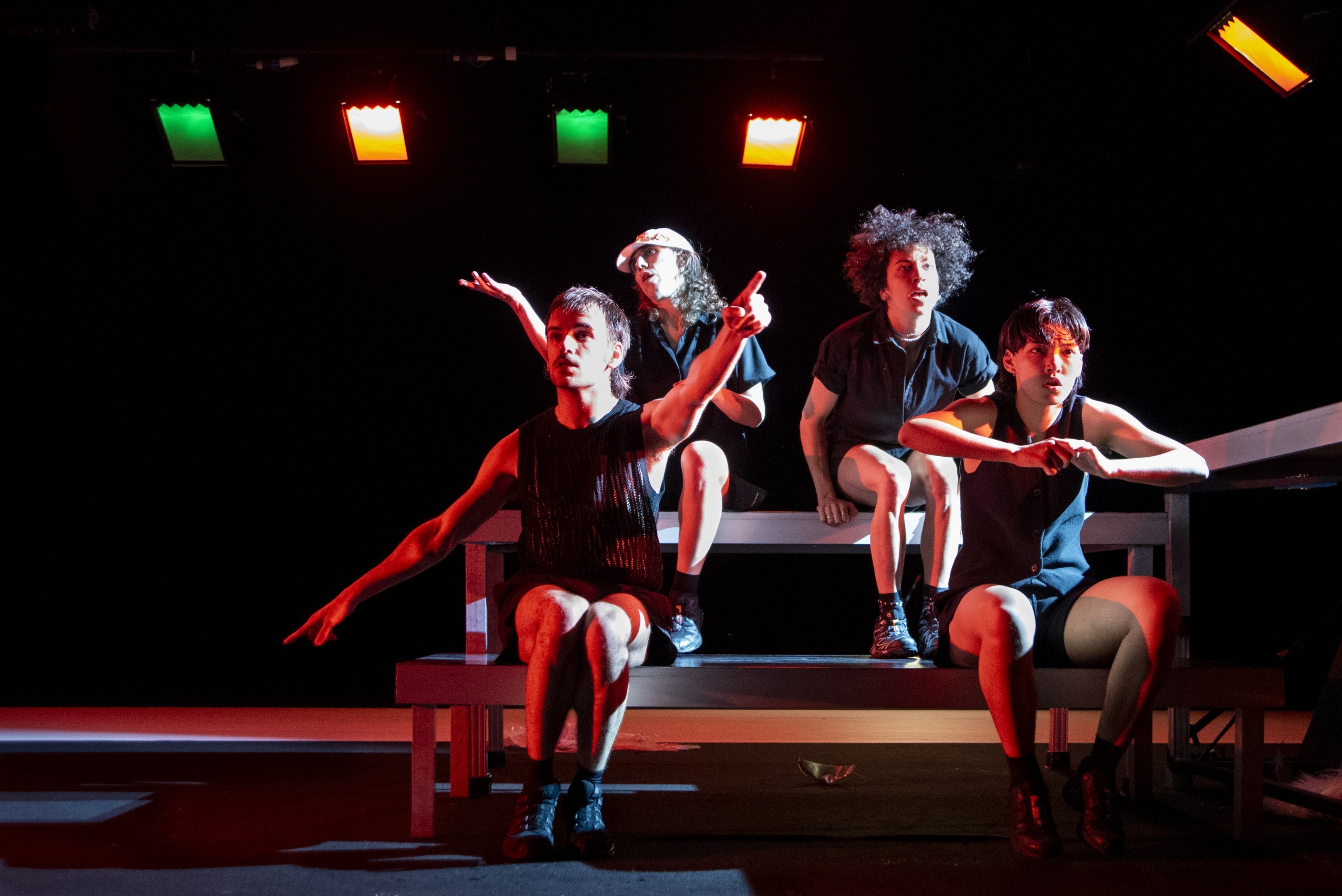 4 dancers sitting on steps in red LED light, one dancer pointing