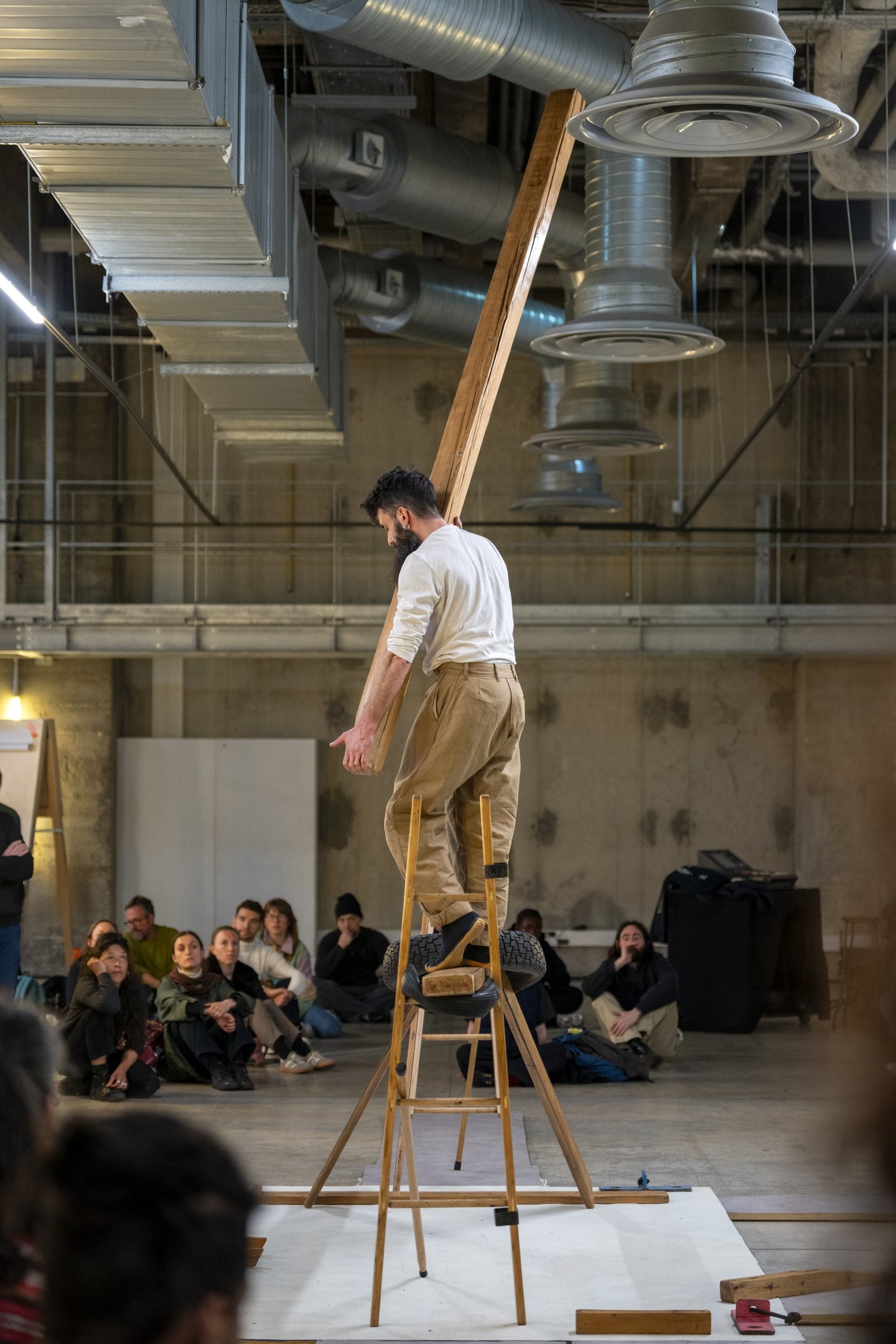 A man on a wooden stepladder holding a wooden beam