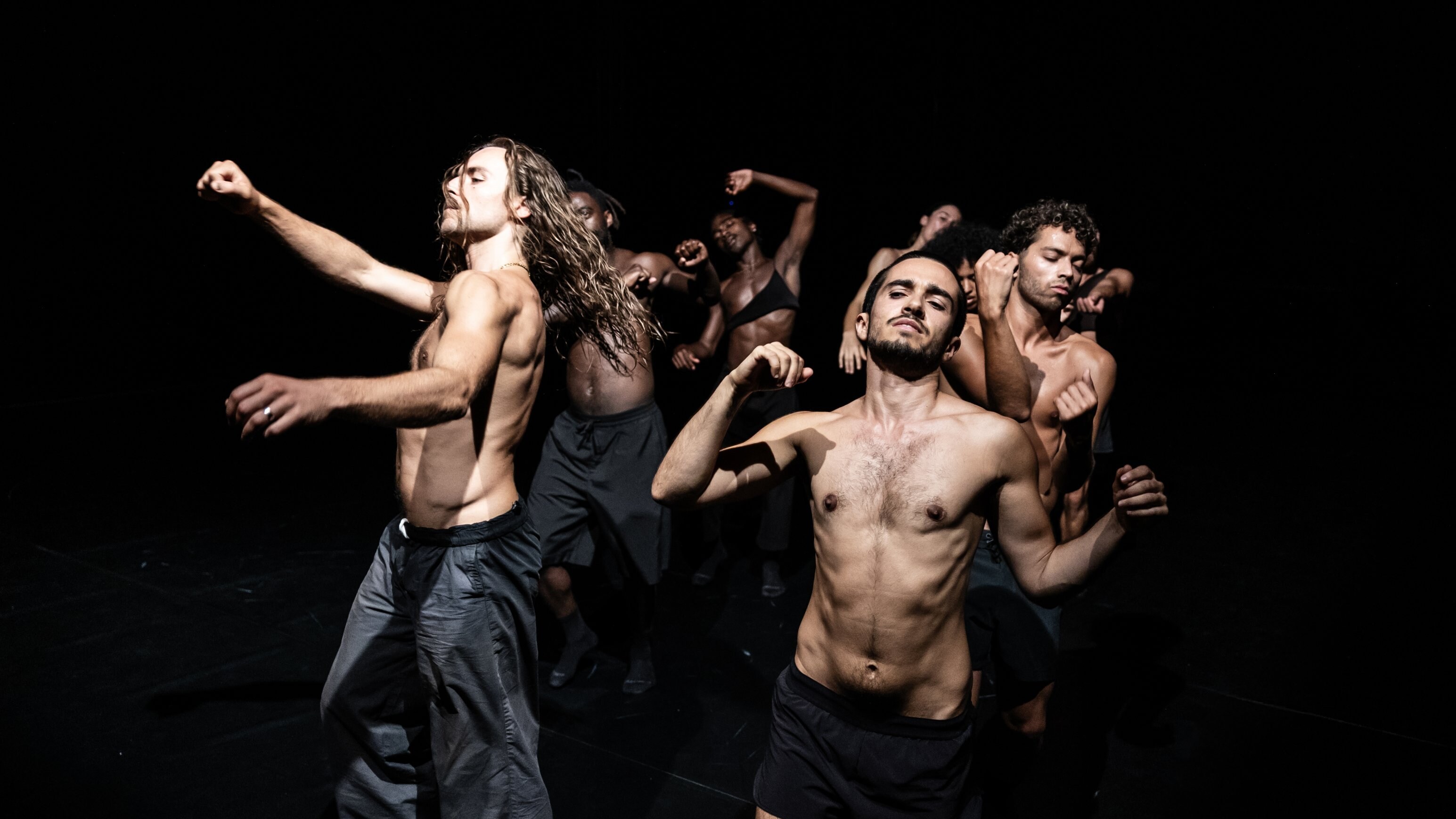 five shirtless dancers in motion in a black background