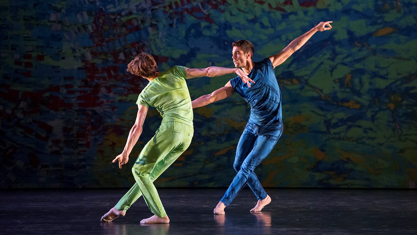 Deux hommes, un en costume vert, l'autre en costume bleu sur scène.