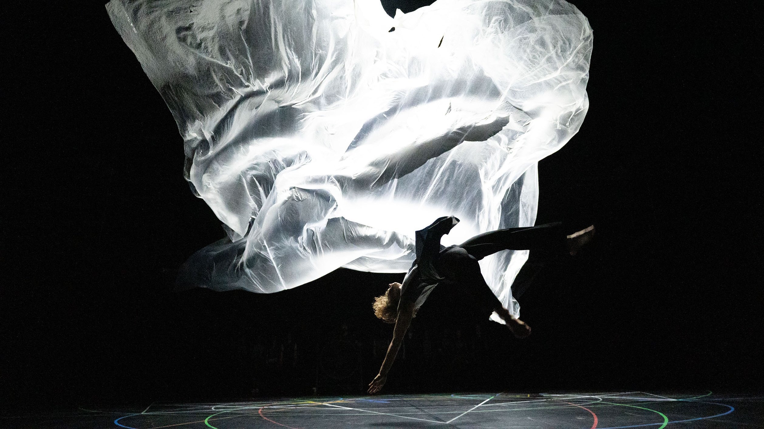 A dancer falling backward, a large white fabric floating behind him.