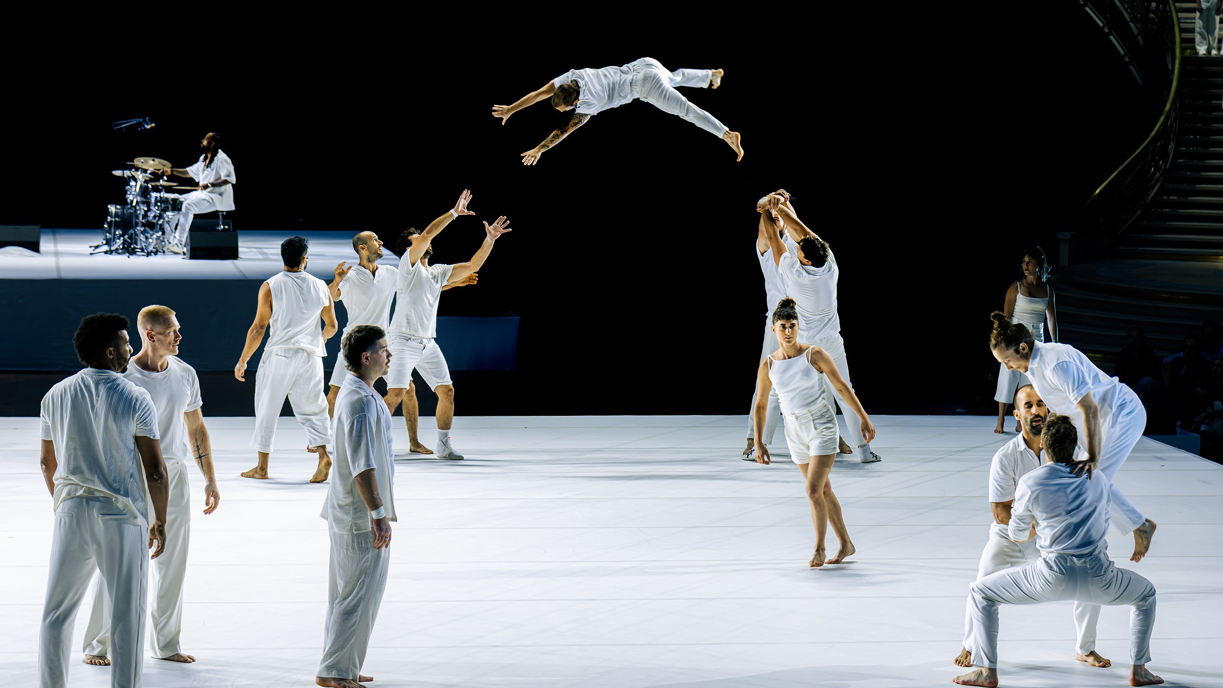 Dancers dressed in white, one in mid-leap