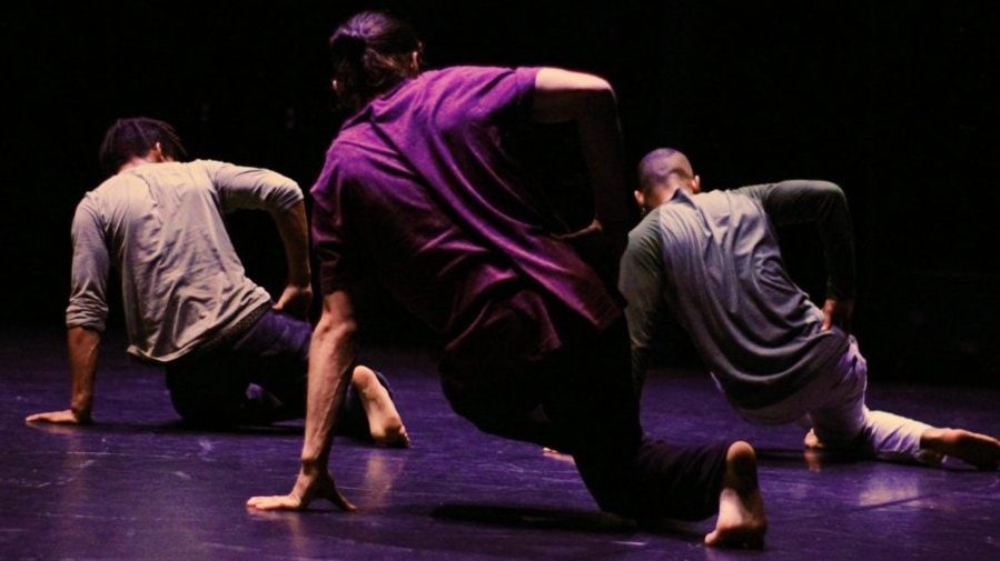 Three dancers seen from the back executing the same move on the floor