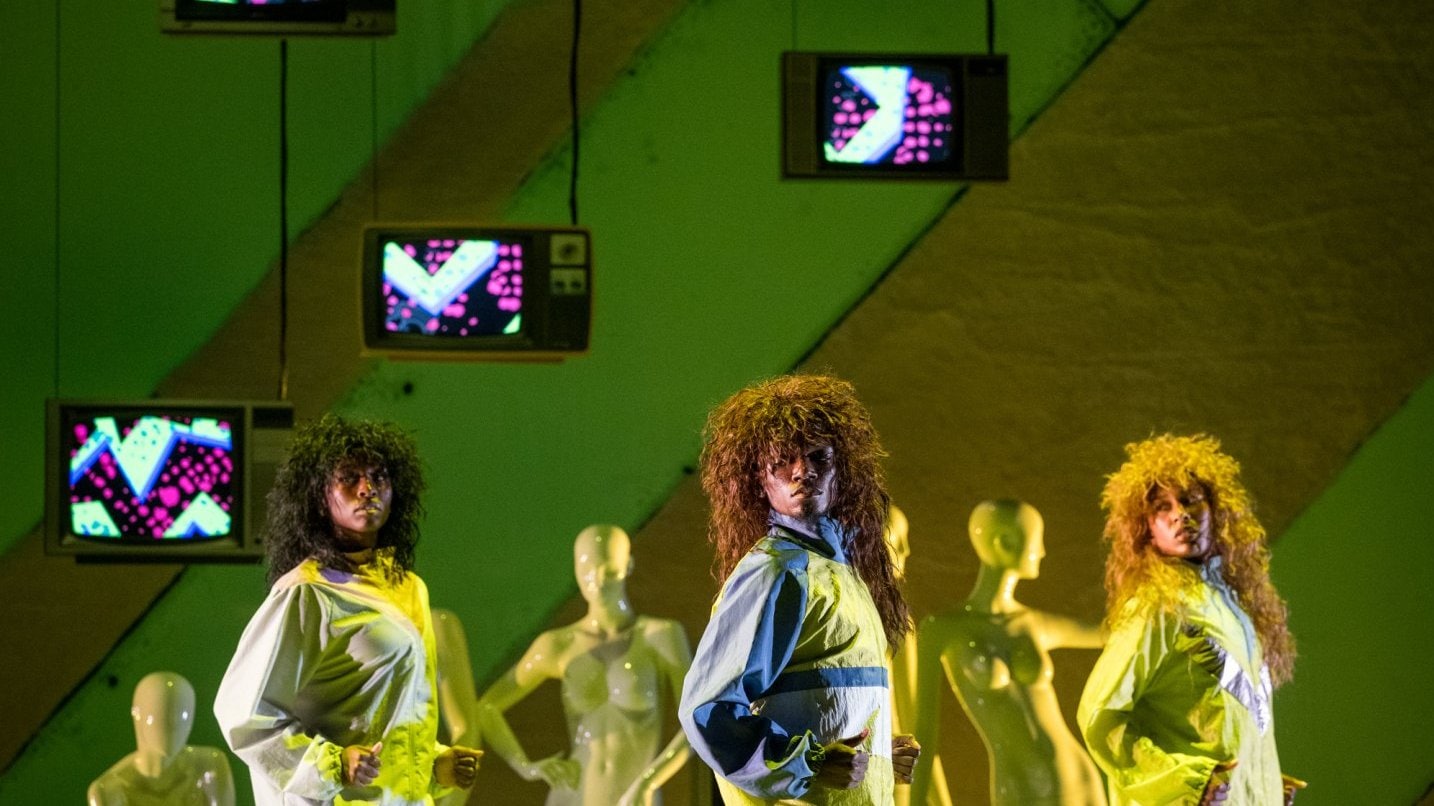 3 dancers on stage in yellow light in front of mannequins