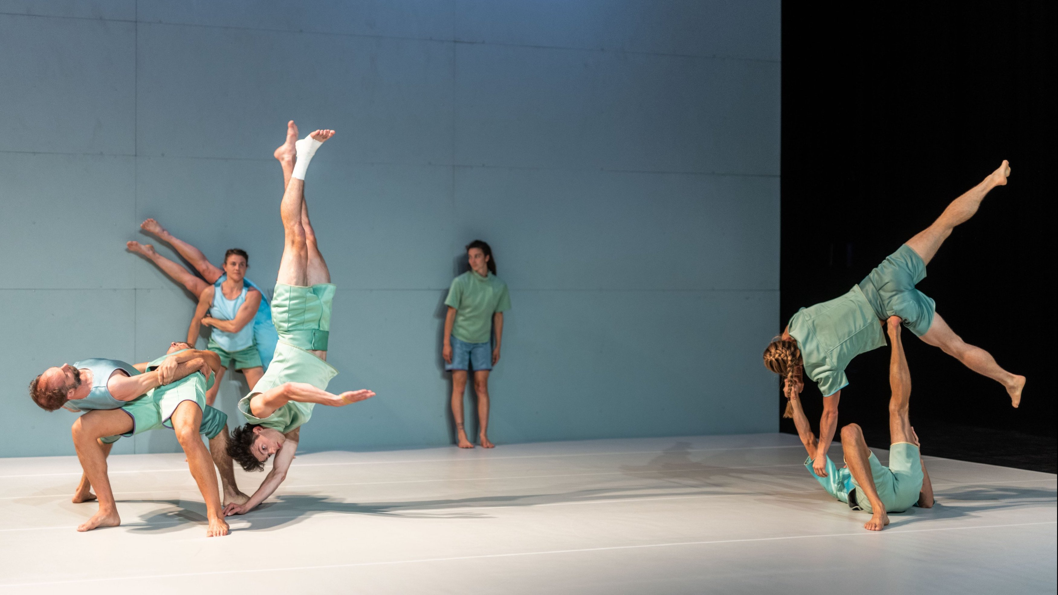 Dancers in light-colored outfits performing lifts and acrobatic figures on stage