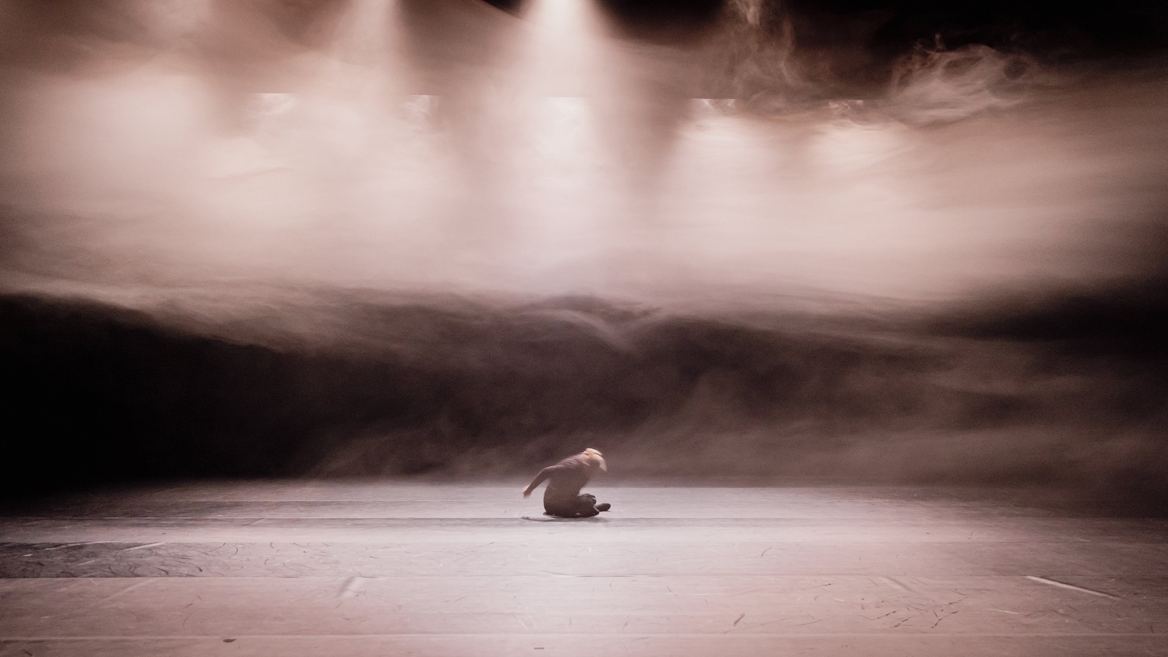 Dancer sitting in mist, under spotlights