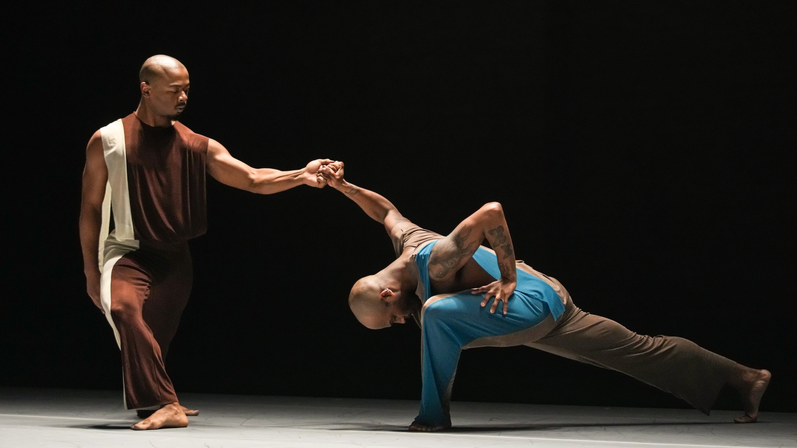 Dancer duo: one standing holding hand of the other in a lunge