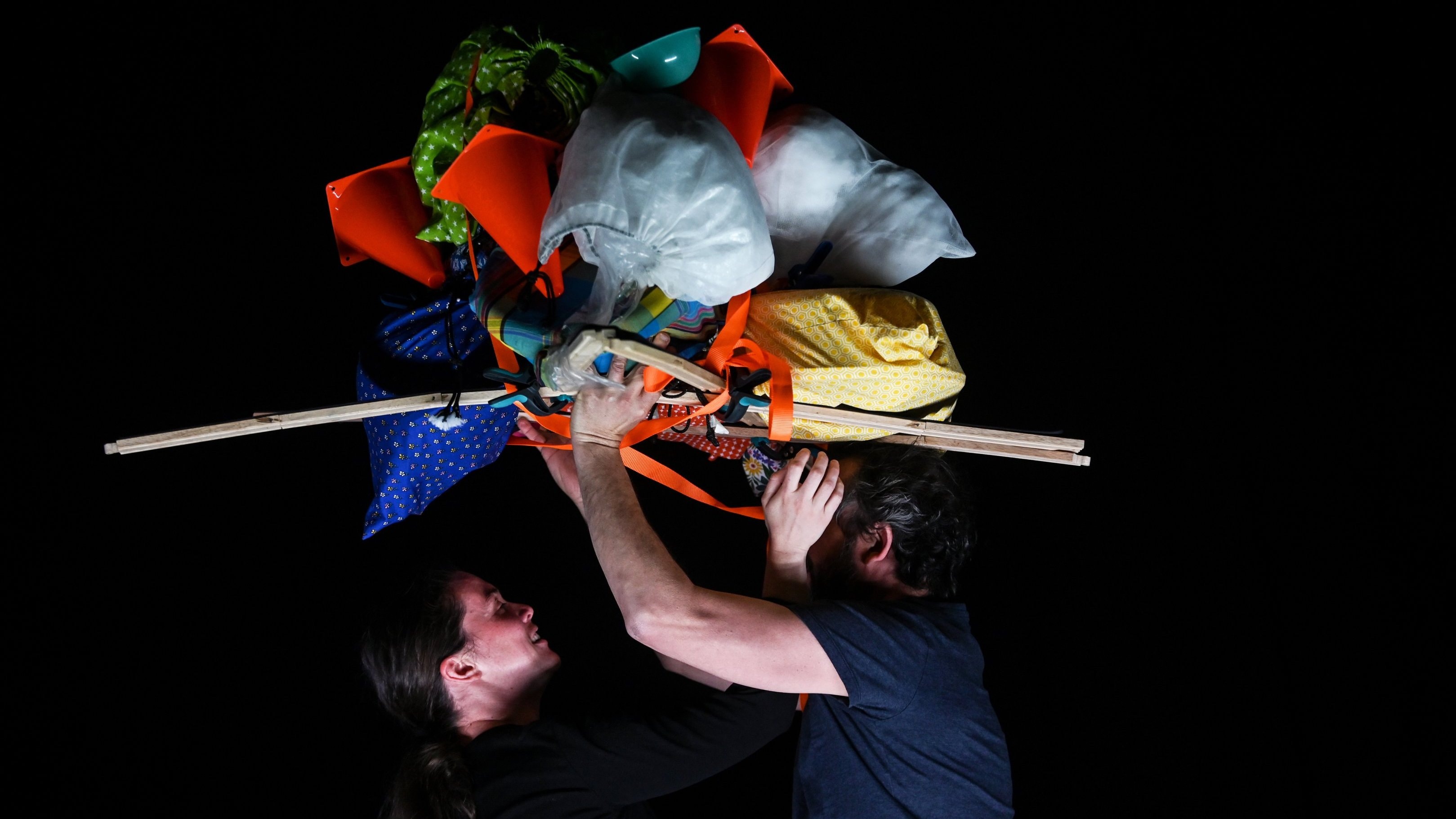 Two people supporting a large, colorful, and varied load of objects