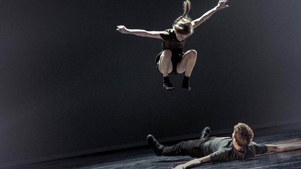 Dancer jumping over a dancer lying down, both dressed in black