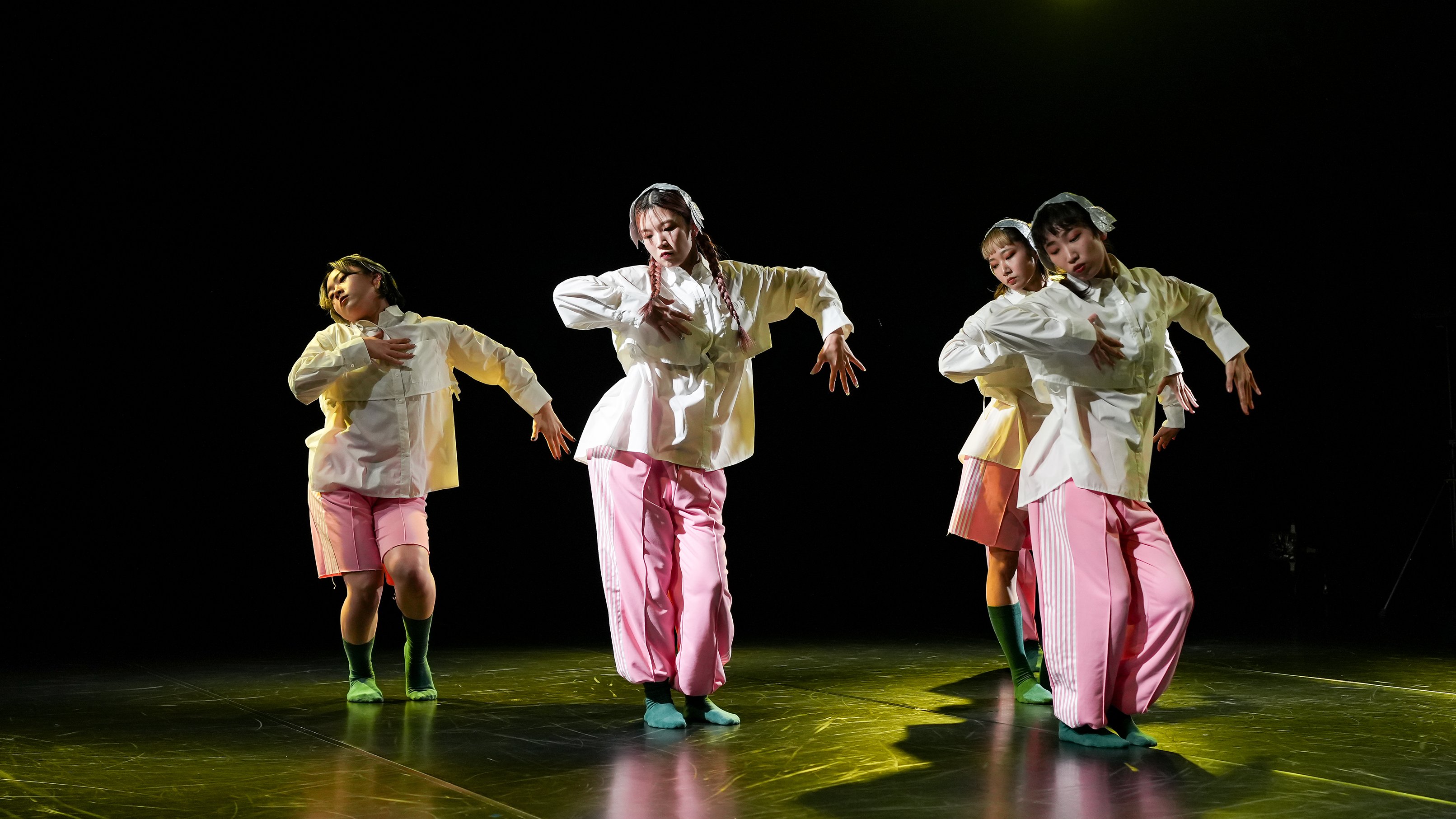 4 dancers dressed in white tops and pink pants standing with their arms bent at right angles
