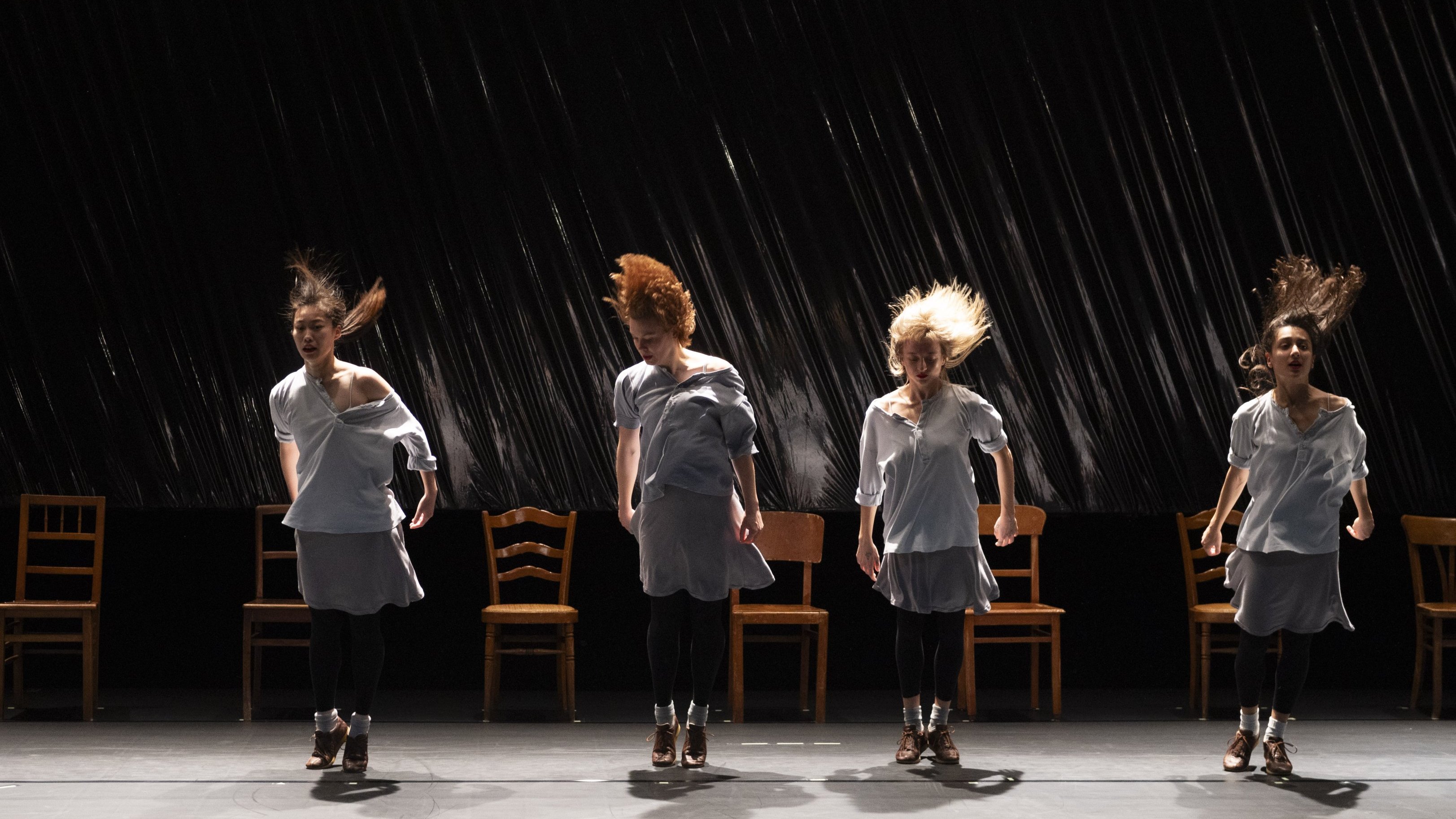 Quatre danseuses en mouvement alignées devant quatre chaises 