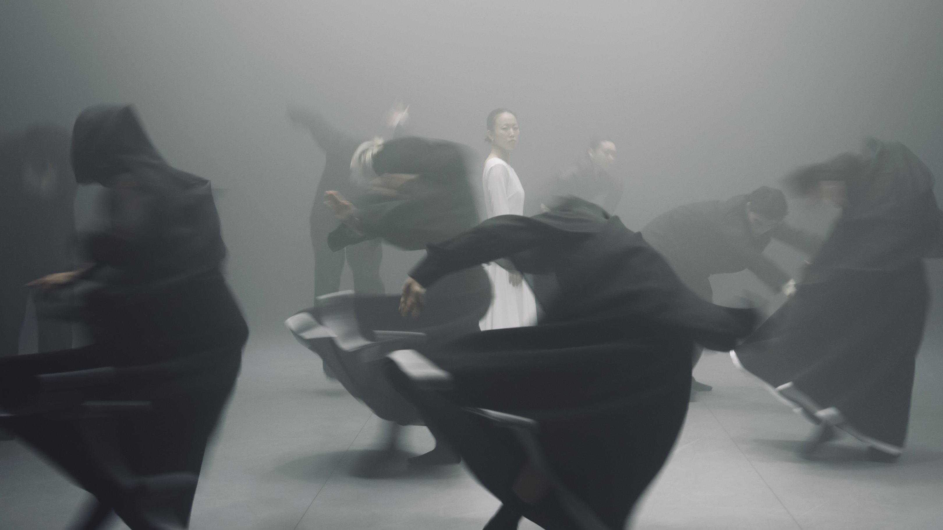 Danseurs en tenue noire  en mouvement tournant autour d'une danseuse dans une tenue blanche. 